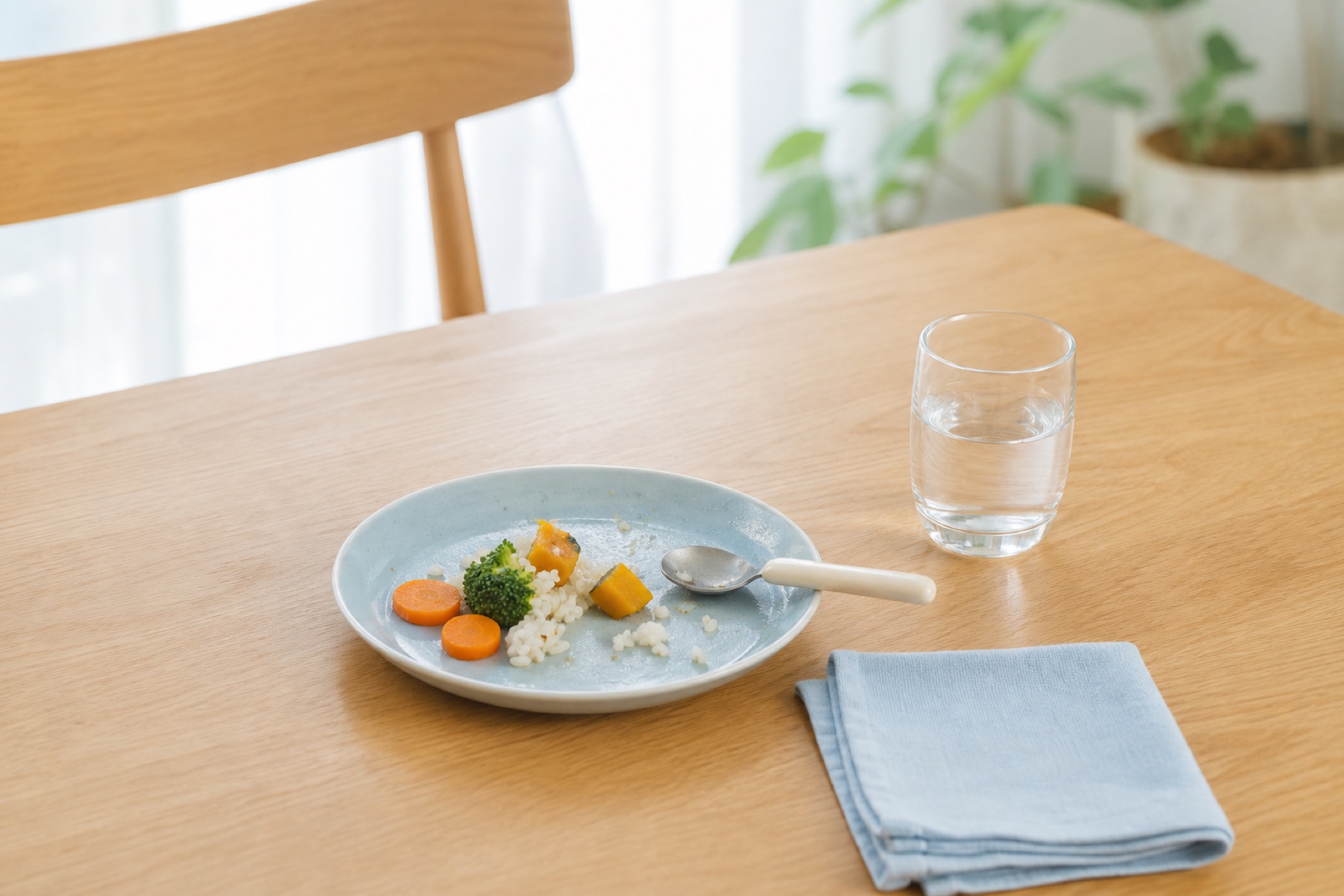 少し食べ物が残った子どもの皿と水を置いた明るい食卓