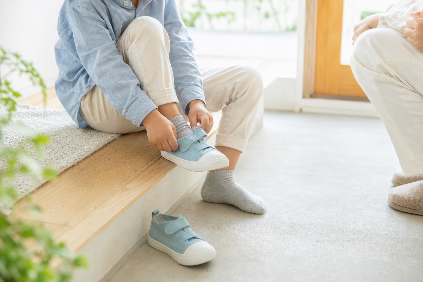 玄関で水色の靴を自分で履く子どもをそばで待つ大人