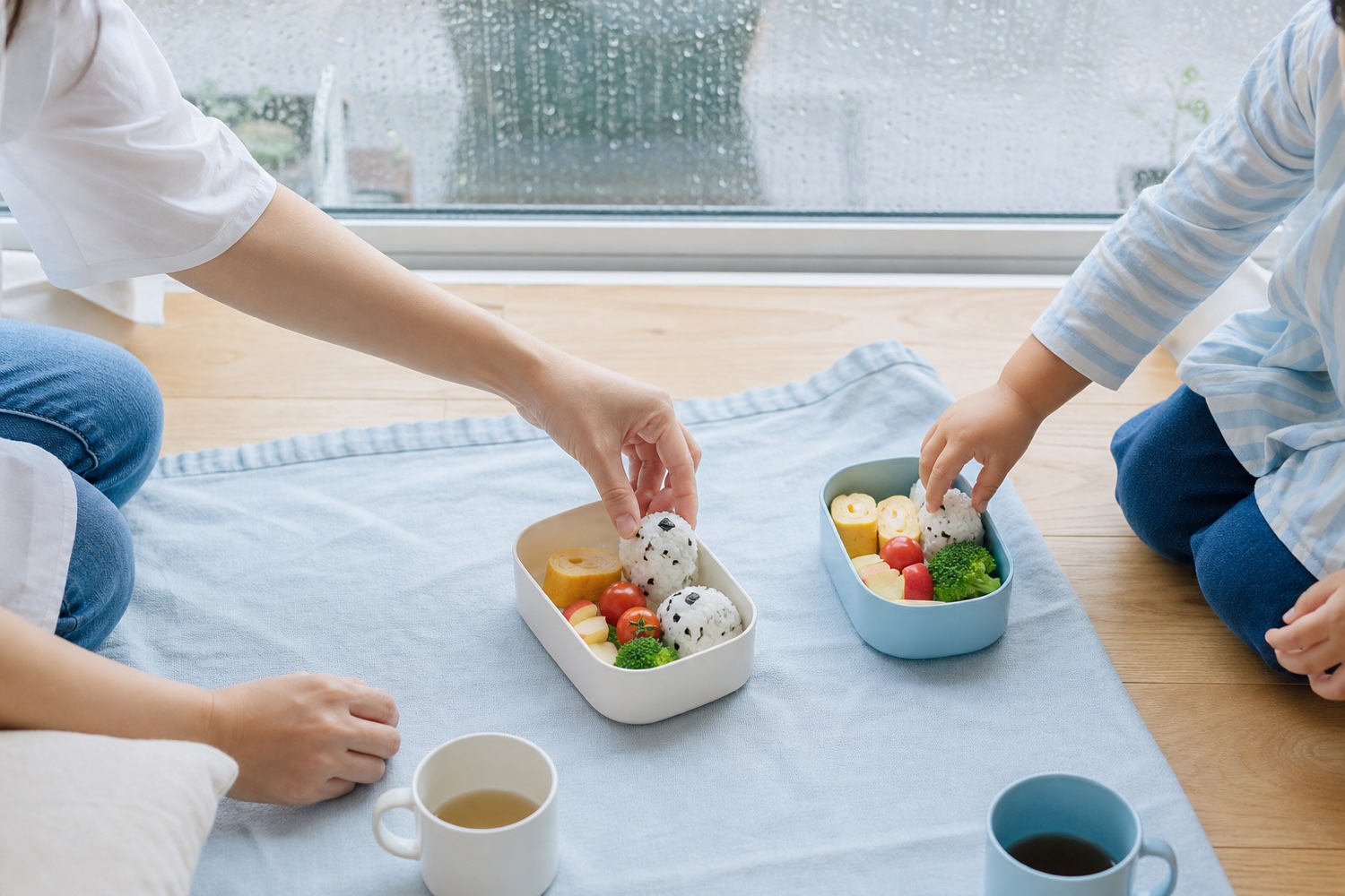 雨の日に家の中でお弁当を楽しむ親子の手元